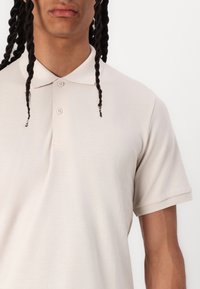 Polo beige con colletto classico, maniche corte e pattina con due bottoni. Tessuto strutturato con dettagli di cucitura sottili.