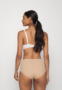 Weißer BH mit verstellbaren Trägern und einem hellbraunen, hochgeschnittenen Slip. Glattes Material, minimalistisches Design und nahtlose Kanten.
