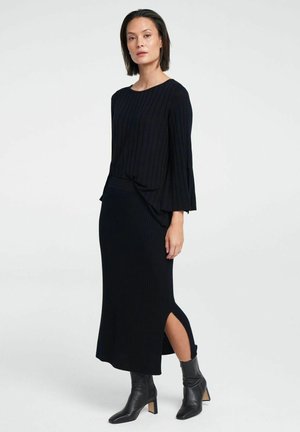 Black ribbed knit top with flared sleeves, paired with a matching ribbed skirt featuring side slits; worn with black heeled ankle boots.