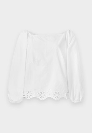 Blusa bianca a maniche lunghe con maniche a sbuffo e orlo ondulato. Presenta un motivo floreale a intaglio lungo il bordo inferiore e una leggera lucentezza.