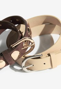 To bælter: et brunt ruskind med store gulddetaljer og spænde; et beige læder med et sølvspænde og minimal dekoration.