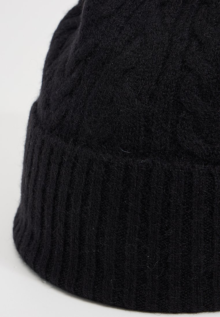 Czarna dziana czapka z mankietem ściągaczem, z akcentem w postaci teksturowanego wzoru w warkocze. Materiał wydaje się miękki i lekko puszysty.