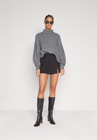 Grijze oversized trui met een hoge hals, gecombineerd met een strakke zwarte minirok met een zijspleet. Kuitlange zwarte leren laarzen.