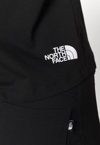 Vêtements noirs avec le logo The North Face imprimé en blanc sur le t-shirt et une petite étiquette en tissu sur la poche du pantalon.