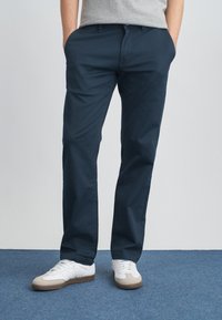 Ναυτικό μπλε βαμβακερά chino με ίσια γραμμή, με πλαϊνές τσέπες. Συνδυασμένα με λευκά αθλητικά παπούτσια και γκρι μπλουζάκι. Απλός σχεδιασμός.