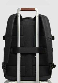 Zaino in tessuto nero con schienale imbottito, spallacci regolabili e maniglia per bagagli in alluminio. Include un dettaglio in pelle sulla maniglia.