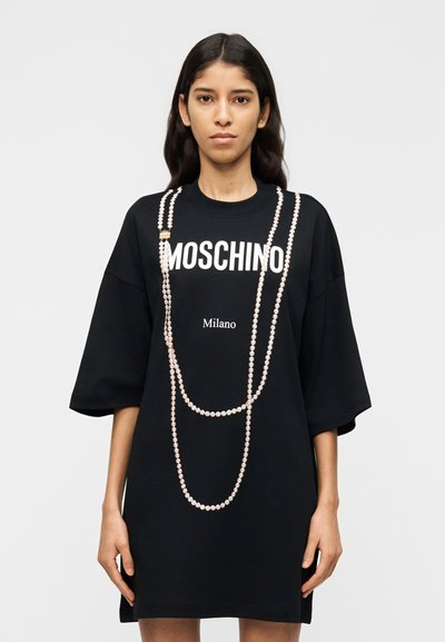 T-shirt noir oversize avec les inscriptions blanches "MOSCHINO" et "Milano", ornée de détails en perles imitant des perles disposées sur le devant.