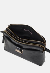 Schwarze, texturierte Lederhandtasche mit zwei offenen goldenen Reißverschlüssen, einem vorderen Riemen mit goldener Schnalle und einem Stoffinnenschild.