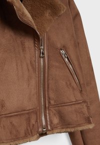 Giacca in pelliccia ecologica marrone con chiusura a zip e tasche laterali. Tessuto morbido con una finitura liscia e colletto a contrasto.