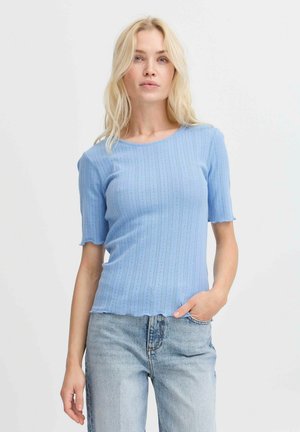 Lichtblauw geribbeld gebreid topje met korte mouwen, gegolfde zoom en subtiel textuurpatroon, gecombineerd met lichtgewassen jeans.
