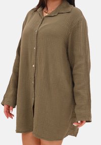 Olivengrøn langærmet skjorte med krøllet tekstur, knappelukning foran og klassisk krave. Sideslidser giver bevægelsesfrihed.