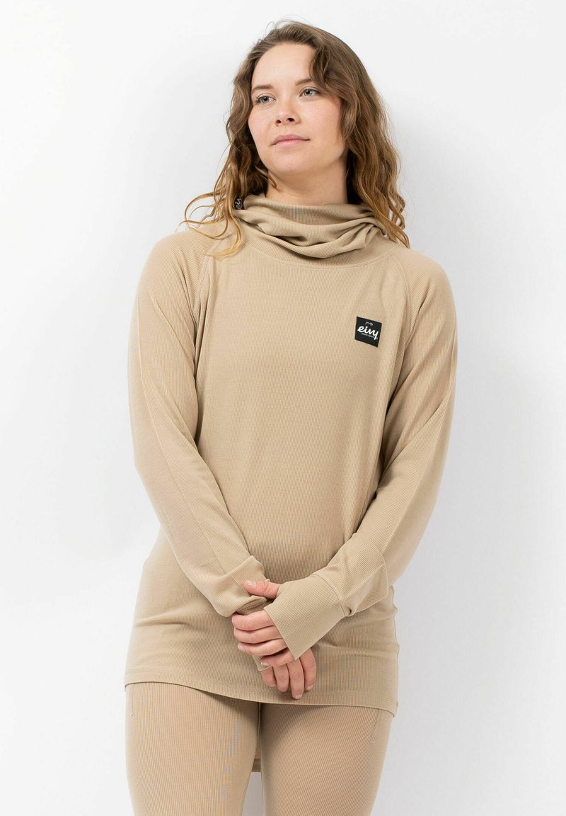 Beige lange mouw top met een colkraag, geribbelde structuur en een label aan de linkerkant. Zachte stof en ontspannen pasvorm, gecombineerd met bijpassende legging.