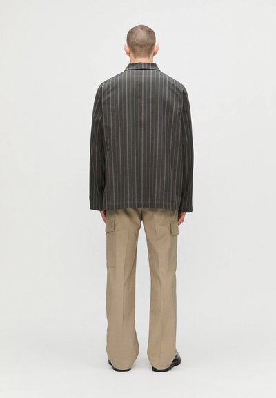 Blazer à rayures sombres avec une coupe décontractée, associé à un pantalon cargo beige. Dispose d'un col et de deux poches latérales sur le pantalon.