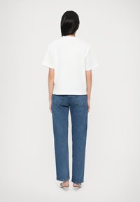 Άσπρο κοντομάνικο T-shirt συνδυασμένο με μπλε τζιν παντελόνι ίσιας γραμμής· μινιμαλιστικός σχεδιασμός, απαλό ύφασμα και εμφανείς ραφές στο τζιν.