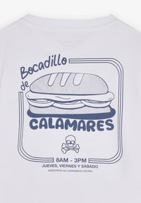 Camiseta blanca con un gráfico azul de un sándwich que muestra un pan superior y el relleno, con texto que detalla horas y contenido, incluyendo un ícono de calavera.