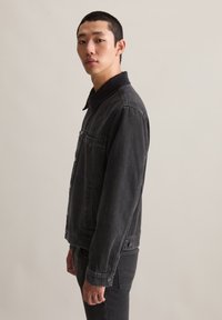 Zwarte denimjacket met dubbele borstzakken, knoopsluiting aan de voorkant en een kraag. Heeft een gestructureerde afwerking en lichte vervaging.