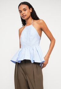 Svetlomodrý halter peplum top s rozšíreným lemom, vyrobený z textúrovanej látky; má tenké ramienka a zips na boku.