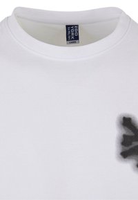 White cotton t-shirt with a round neckline and a dark gray graphic detail on the front. Tag reads "Zoo York" in blue.