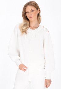 Weißer Strickpullover mit Rundhalsausschnitt, gerippten Bündchen und dekorativen goldenen Knöpfen auf der Schulter. Weiche Textur und lockere Passform.