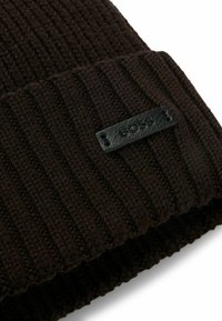 Brown ribbed knit beanie with a folded cuff, featuring a black leather tag embossed with "BOSS" attached at the front.