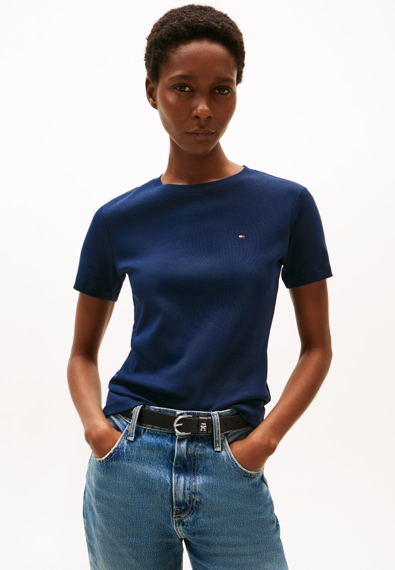 Navy blue short-sleeve t-shirt with a round neck and a small logo. Worn with light blue denim jeans and a black belt featuring a silver buckle.