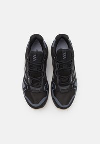 Černé sportovní boty s síťovaným materiálem, gumovými podrážkami a šedými akcenty. Mají zesílenou špičku a šněrovací systém pro bezpečné uchycení.