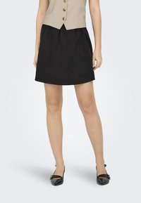 Sort skjørt med en glatt tekstur og A-linjeshape, kombinert med blanke svarte leiligheter som har to dekorative stropper og en liten sløyfedetalj.