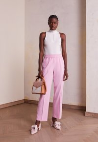 Vit ärmlös topp med dragkedja, rosa byxor med elastisk midja, glittriga rosa skor prydda med rosett, samt en handväska i tan och ljusrosa.