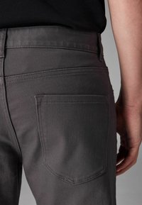 Grå denimjeans med en tætsiddende silhuet, som har en baglomme og diskrete stikninger. Materialet er glat med en let glans.