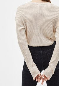 Beige geribbelde trui met lange mouwen, relaxte pasvorm en hoge hals. Gecombineerd met zwarte high-waisted jeans, met achterzakken.