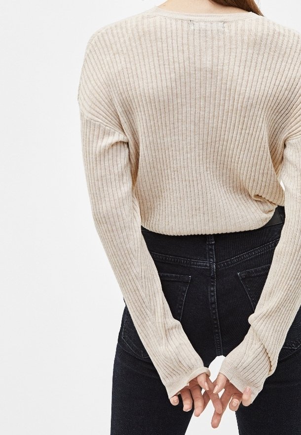 Beige geribbelde trui met lange mouwen, relaxte pasvorm en hoge hals. Gecombineerd met zwarte high-waisted jeans, met achterzakken.