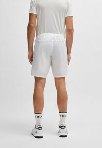 Pantalones cortos deportivos blancos con una cintura elástica y un tejido suave y ligero. El modelo también lleva calcetines blancos con detalles en negro y zapatillas.