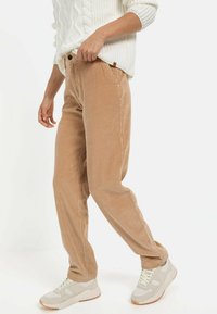 Beige corduroy bukser med ribbet tekstur, afslappet pasform og frontlommer, parret med lyse sneakers.