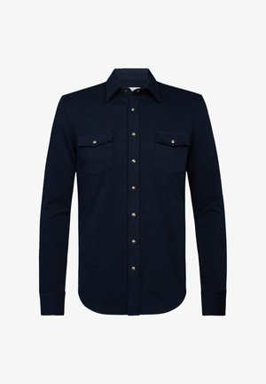 Camisa de manga larga azul marino hecha de una tela suave. Presenta dos bolsillos en el pecho con solapas con botón, botones plateados en el frente y un cuello clásico.