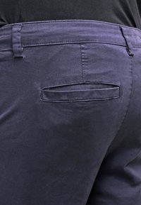 Námořnické modré chinos kalhoty s zadní kapsou s obdélníkovým klopou, vyrobené z hladké tkaniny s minimální texturou. Viditelné stylové švy.