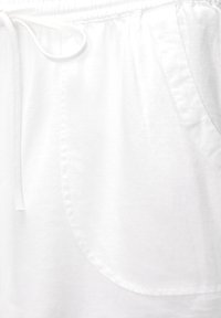 Bílé bavlněné kraťasy s elastickým pasem, šňůrkou a bočními kapsami. Tkanina se zdá být měkká a lehká s hladkým povrchem.