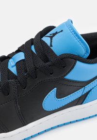 Černé kožené tenisky s modrými akcenty, včetně swooshe a jazyka. Mají černé tkaničky, texturovaný svršek a bílou podrážku s modrým lemováním.