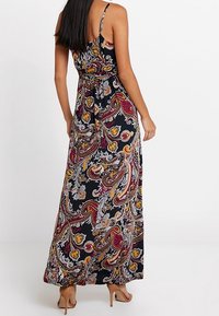 Robe maxi avec bretelles fines, fond noir, motif paisley multicolore en rouge, jaune et blanc. Le tissu est léger et fluide.