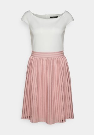 Haut blanc ajusté à manches courtes avec un col bateau, associé à une jupe plissée rose taille haute avec des motifs verticaux.
