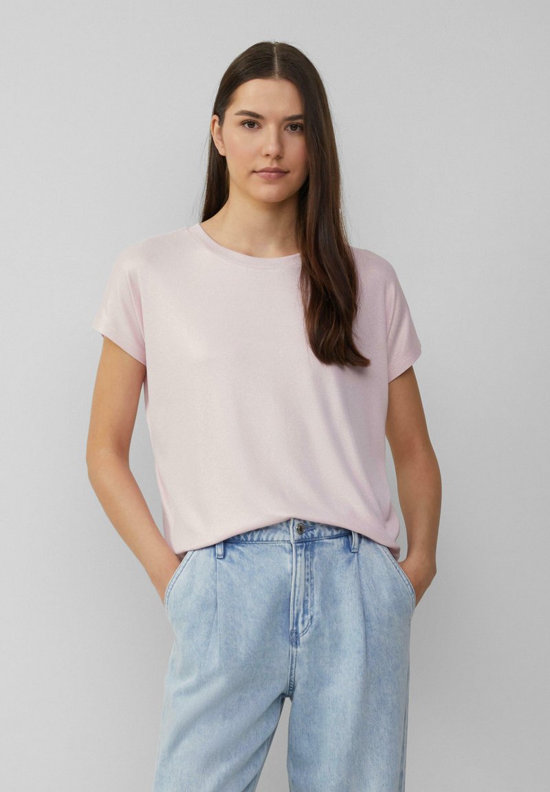 Rosa T-Shirt mit kurzärmeligen, runder Ausschnitt, aus glattem Stoff, kombiniert mit hellblauen hoch geschnittenen Jeans. Das Model steht mit den Händen in den Taschen.