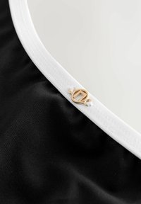 Sort stof med glat tekstur, med hvid kant og en guldfarvet cirkulær metal detalje med en logoaccent.