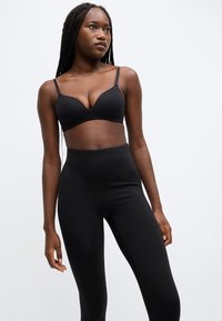 Bralette negru cu bretele subțiri și decolteu adânc, asortat cu colanți negri cu talie înaltă, dintr-un material neted și elastic.