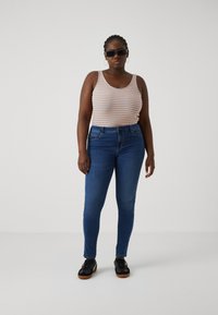 Striped tank top in orange, blue, and white; blue slim-fit jeans; black sneakers with gum soles; round sunglasses; hoop earrings.