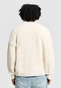 Cream-colored fleece sweater with a soft texture, dropped shoulders, and ribbed cuffs. Features a relaxed fit with a plain backing.