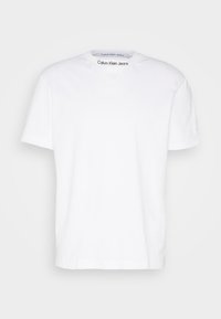 Camiseta de algodón blanca con cuello en V, mangas cortas y un logo en la manga izquierda. Textura suave, diseño casual y líneas limpias.