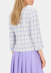 Tkanina blazer w niebiesko-białą kratę z rękawami o długości trzech czwarte i postrzępionymi mankietami, w połączeniu z plisowaną lawendową spódnicą.
