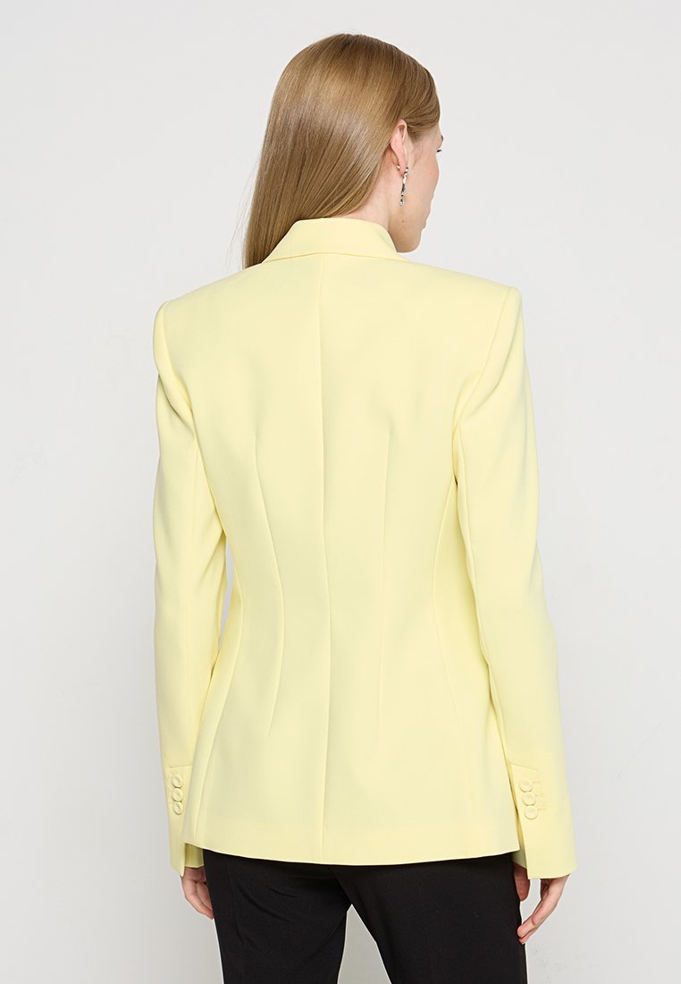 Maßgeschneiderte Blazer in Pastellgelb, strukturierte Silhouette mit gepolsterten Schultern, Ein-Knopf-Verschluss und knöpfbaren Manschetten. Glatte Textur.