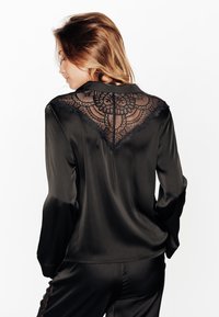 Blouse en satin noir à manches longues, avec des détails en dentelle noire complexe au dos et une texture douce et lisse.