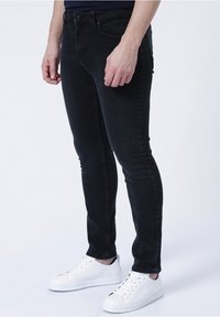 Černé slim džíny s pěti kapsami a knoflíkovým zapínáním, doplněné o bílé tenisky s perforovanými detaily a plochými tkaničkami.