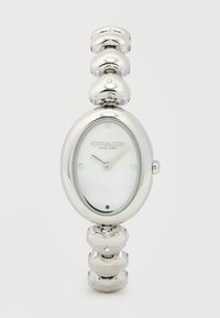 Ασημένιο ρολόι χειρός Coach με οβάλ λευκό καντράν και αλυσίδα σε σχήμα καρδιάς, δείχνει ώρα 11:07.